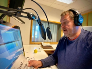 Generalsekretær Øyvind Woie sitter i lydstudio på KABB og leser inn Vårt Land. Han har blå genser, headset på hodet og er ubarbert. 