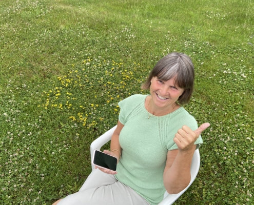 Kjersti Lium sitter i en stol og holder en mobiltelefon på en grønn gressbakke