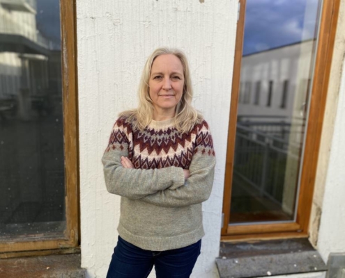 En kvinne i strikket genser foran en vegg