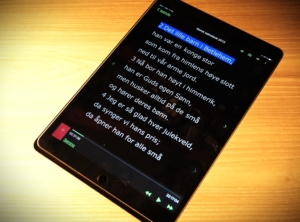En ipad ligger på et bord, skjermen viser salmen "Et barn er født i Betlehem" i hvit skrift på svart bunn. 